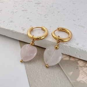 Close-up of golden hoop earrings featuring pink natural stone heart pendants and beads