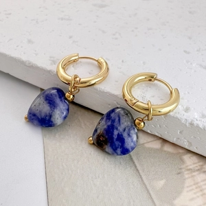 Detail of heart-shaped blue natural stone earrings with gold hoops on stone display