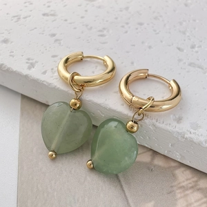 Close-up of heart-shaped green stone earrings with gold hoop on white textured stone
