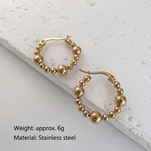 Polished golden stainless steel beaded hoop earrings on a textured stone display