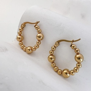 Polished golden stainless steel beaded hoop earrings on light marble surface