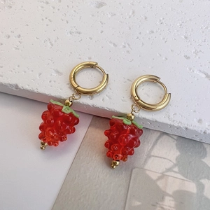 Macro shot of 3D red grape pendants on gold hoops over a textured white stone surface