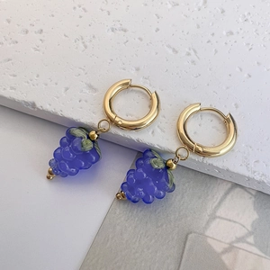 Close-up of golden hoop earrings featuring translucent purple grape cluster pendants