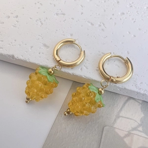 Detail of titanium steel gold earrings with translucent yellow grape-shaped resin pendants