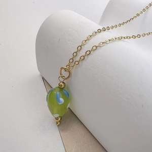 Gros plan sur un collier doré avec pendentif fraise en verre vert fait main