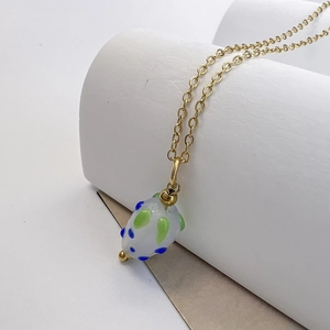 Détail d'un pendentif fraise en verre blanc avec pois bleus sur une chaîne dorée