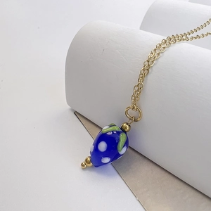 Gros plan détaillé du pendentif fraise en verre bleu à pois blancs sur chaîne dorée