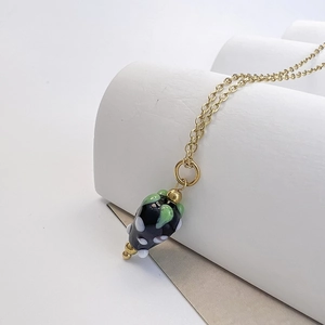 Détail du pendentif fraise en verre avec chaîne en acier doré sur support blanc