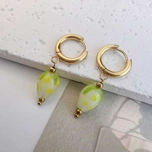 Close-up of green glass strawberry pendant earrings with yellow dots and gold hoops