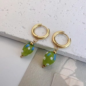Detailed close-up of gold hoop earrings with green glass drop pendants and dot patterns