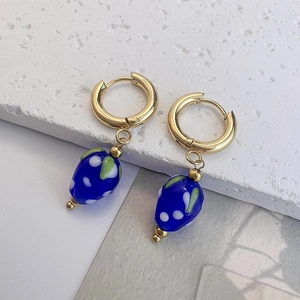 Macro view of strawberry fruit earrings with blue berries and gold hoops on stone
