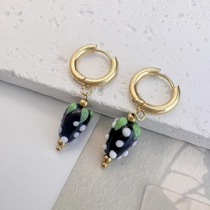Detail of gold strawberry earrings with black and white polka dots on stone plate
