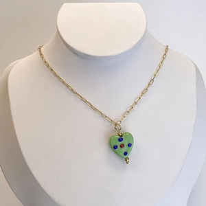 Close-up of green heart pendant with colorful dots on a golden paperclip chain