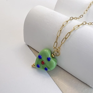 Detail of light green heart pendant on gold chain with colorful dotted accents