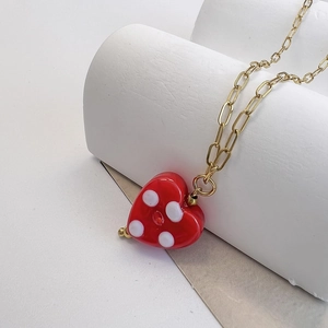 Macro detail of red heart pendant with white polka dots on golden paperclip chain necklace