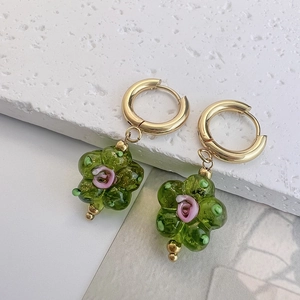 Détail de boucles d'oreilles créoles dorées avec pendentifs fleurs en verre vert et roses