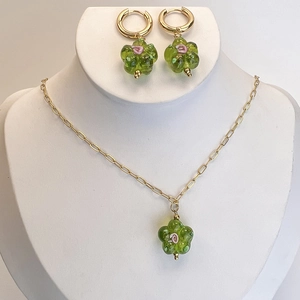 Close-up of green glass flower pendant necklace and earrings set on a white display stand