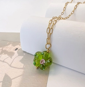 Close-up of green glass flower pendant and gold link chain on white display