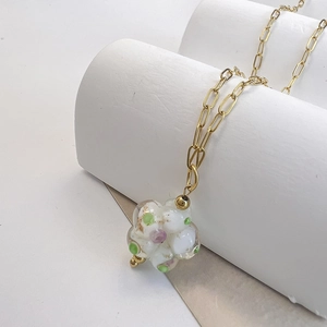 Detailed close-up of a glass floral pendant with gold accents on a stainless steel chain