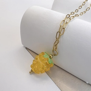 Detailed close-up of a yellow glass berry pendant on a gold paperclip chain necklace