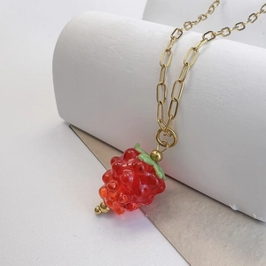 Detailed close-up of a glass raspberry pendant on a gold-plated paperclip chain necklace