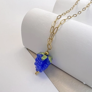 Detail of a purple glass raspberry pendant with green leaves on a gold rectangle chain