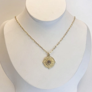 Détail du collier à pendentif soleil doré avec pierre sombre et chaîne de type trombone