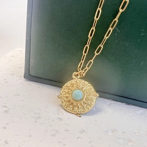 Gros plan du pendentif soleil doré serti de turquoise sur une chaîne trombone