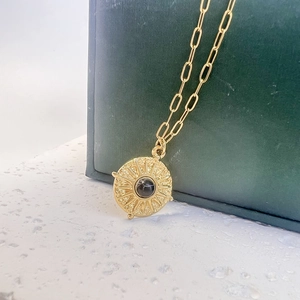 Vue détaillée du pendentif soleil doré avec pierre noire sur une chaîne trombone