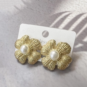 Close-up of golden frosted flower earrings with central pearl on a white display card