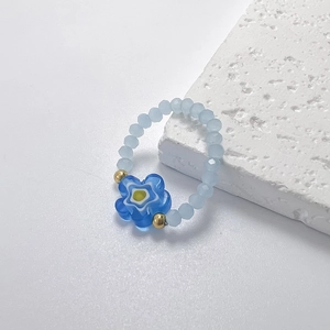 Detail eines hellblauen Perlenrings mit Blumenanhänger und goldenen Akzenten am Rand