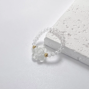Nahaufnahme eines handgefertigten Perlenrings mit weißer Blume und goldenen Details