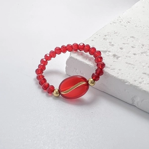 Detail of red beaded elastic ring with gold leaf-textured center stone on stone base