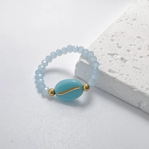 Close-up of light blue glass beaded ring with golden leaf accents on stone background