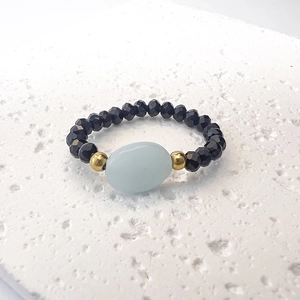 Dettaglio di un anello elastico con perline sfaccettate nere e una pietra centrale blu chiaro