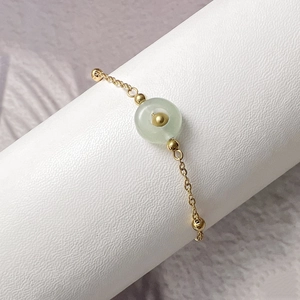 Macro detail of gold-plated titanium steel bracelet featuring a green natural stone charm