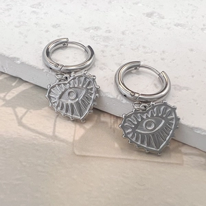 Detalle de pendientes de corazón plateados con motivo de ojo turco sobre base de piedra