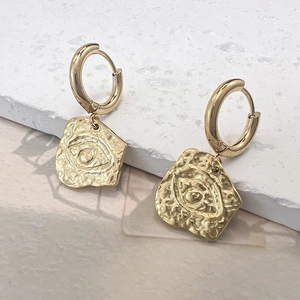 Detalle de pendientes de aro dorados con colgante de ojo y textura martillada fina