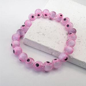 Macro view of pink evil eye beaded bracelet with resin charms on a white stone tile