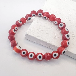 Close-up of red Evil Eye beads bracelet with elastic cord on white marble stone