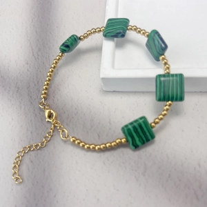 Macro view of gold beaded bracelet featuring green faux malachite stones and lobster clasp
