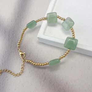 Detail of beaded gold bracelet with green stones on a white tray and purple background