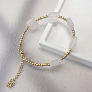 Detail of bohemian gold beaded bracelet with pink natural stones and heart charm