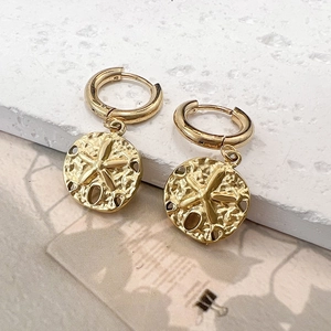 Detailed macro of gold starfish drop earrings with star pattern and hammered texture