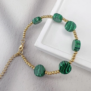 Gros plan de perles dorées 18K et pierres de malachite verte sur bracelet avec fermoir homard
