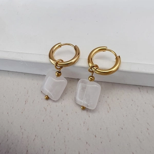 Detailed macro view of 18K gold hoops with square translucent white stone pendants