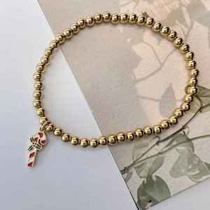 Detail of golden beaded elastic bracelet featuring a red and white candy cane charm