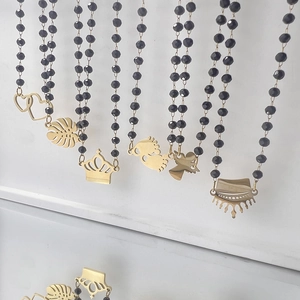 Beaded black necklace with various gold charms like heart and monstera leaf pendants