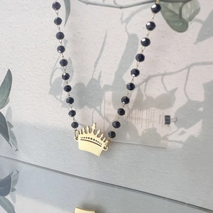 Macro shot of gold crown pendant and black faceted beaded chain necklace