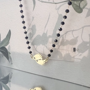 Detail of golden baby feet pendant on black faceted beaded necklace with soft shadows